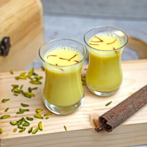 Turmeric and saffron milk on a rustic wooden board, garnished with pistachios.