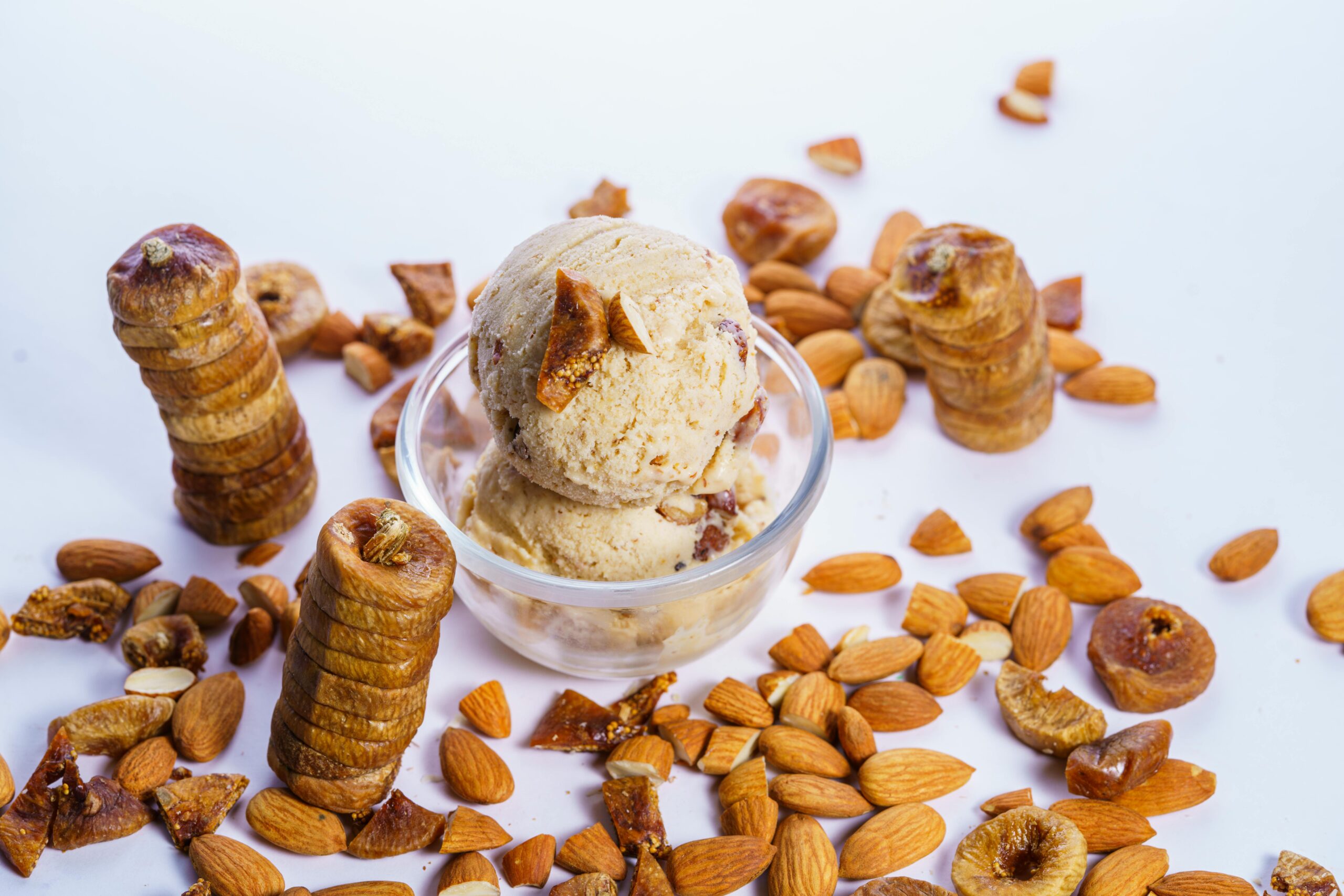 Scoops of almond fig ice cream in a glass bowl surrounded by almonds and figs.