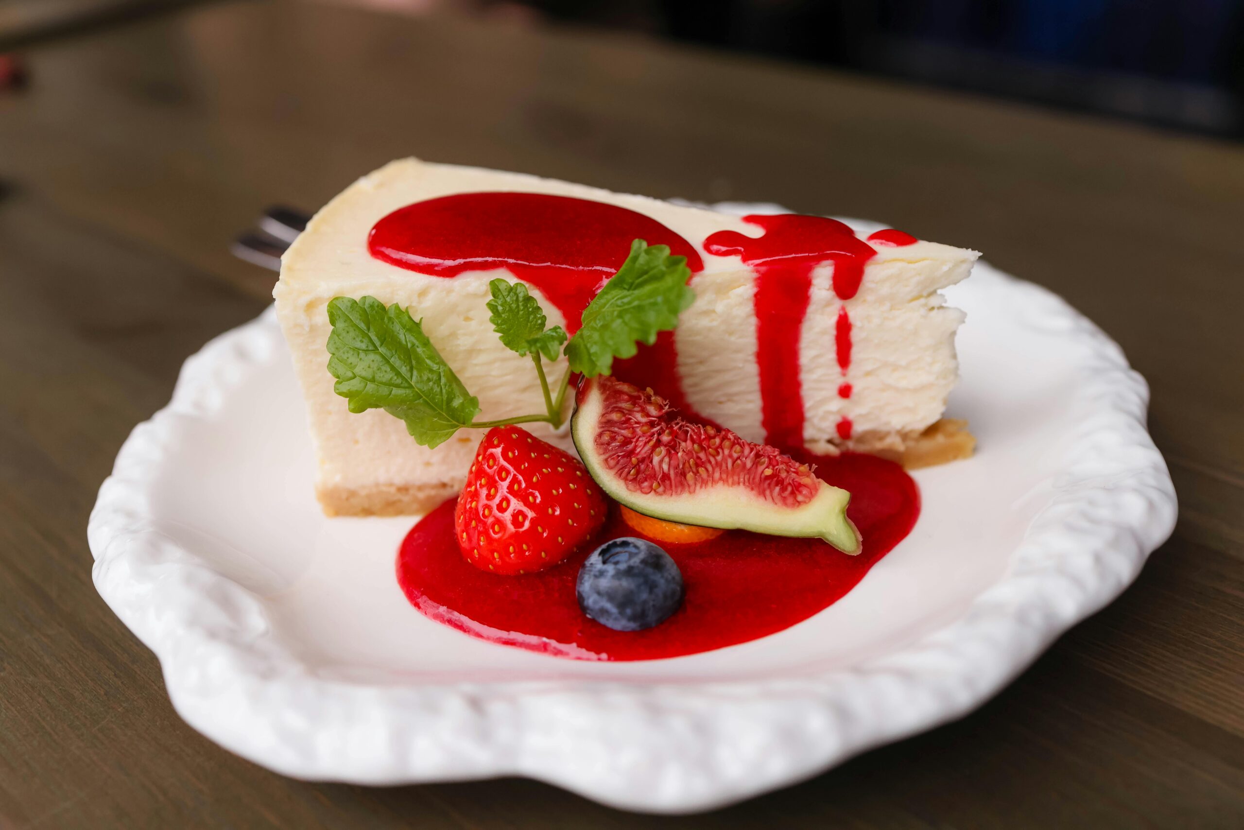 Cheesecake with fig, strawberry, blueberry, and raspberry sauce on a white plate.