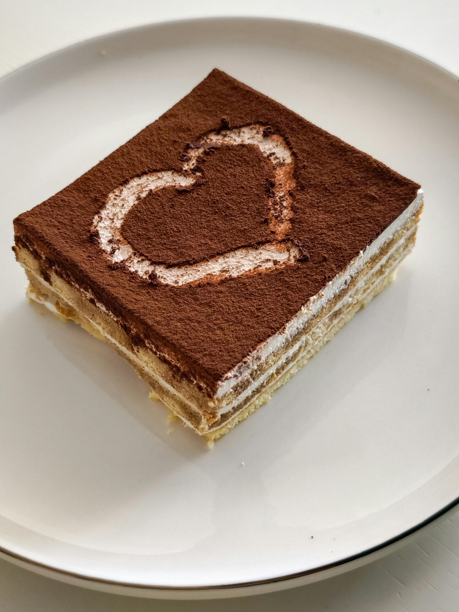 A square slice of tiramisu dessert with a cocoa heart design on top, perfect for romantic occasions.