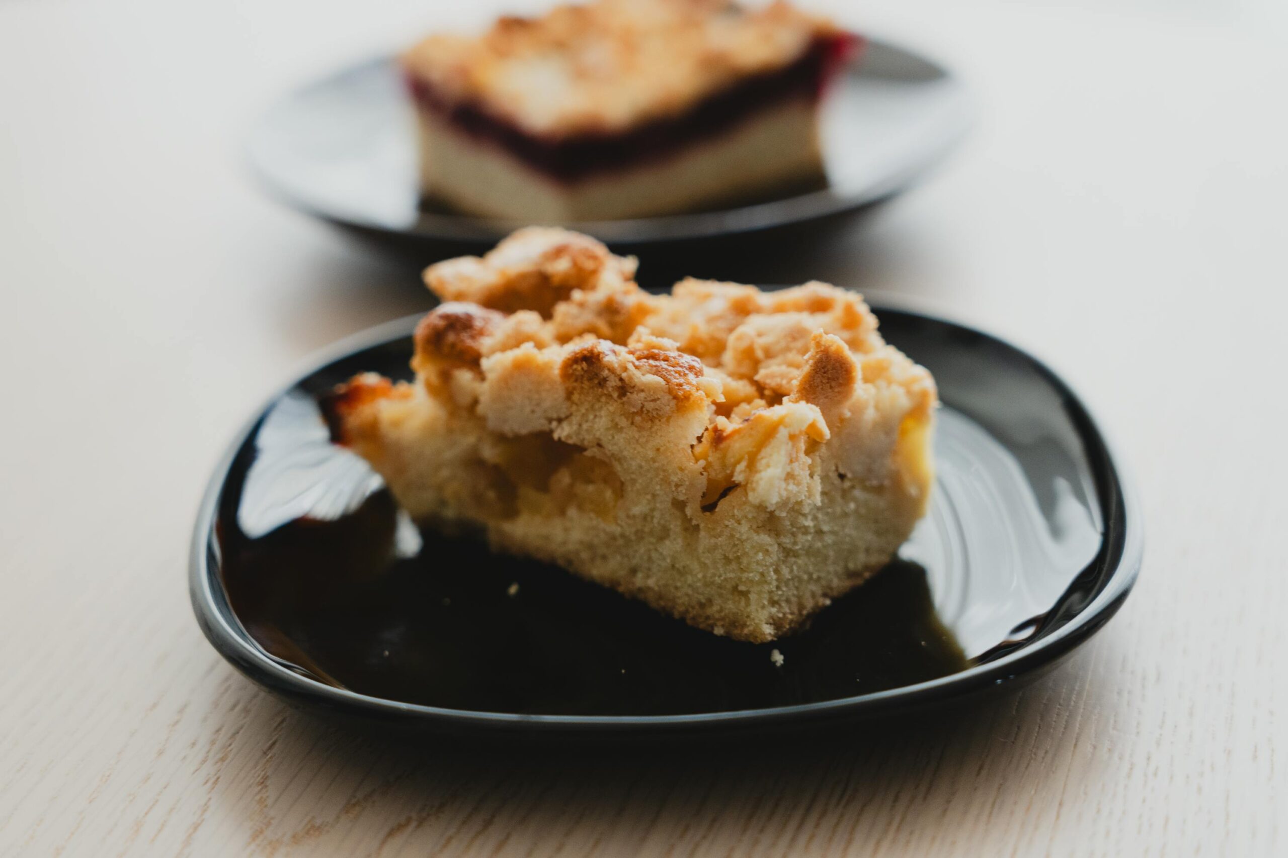 Close-up of a slice of apple streusel cake on a black plate, showcasing its crumbly topping.