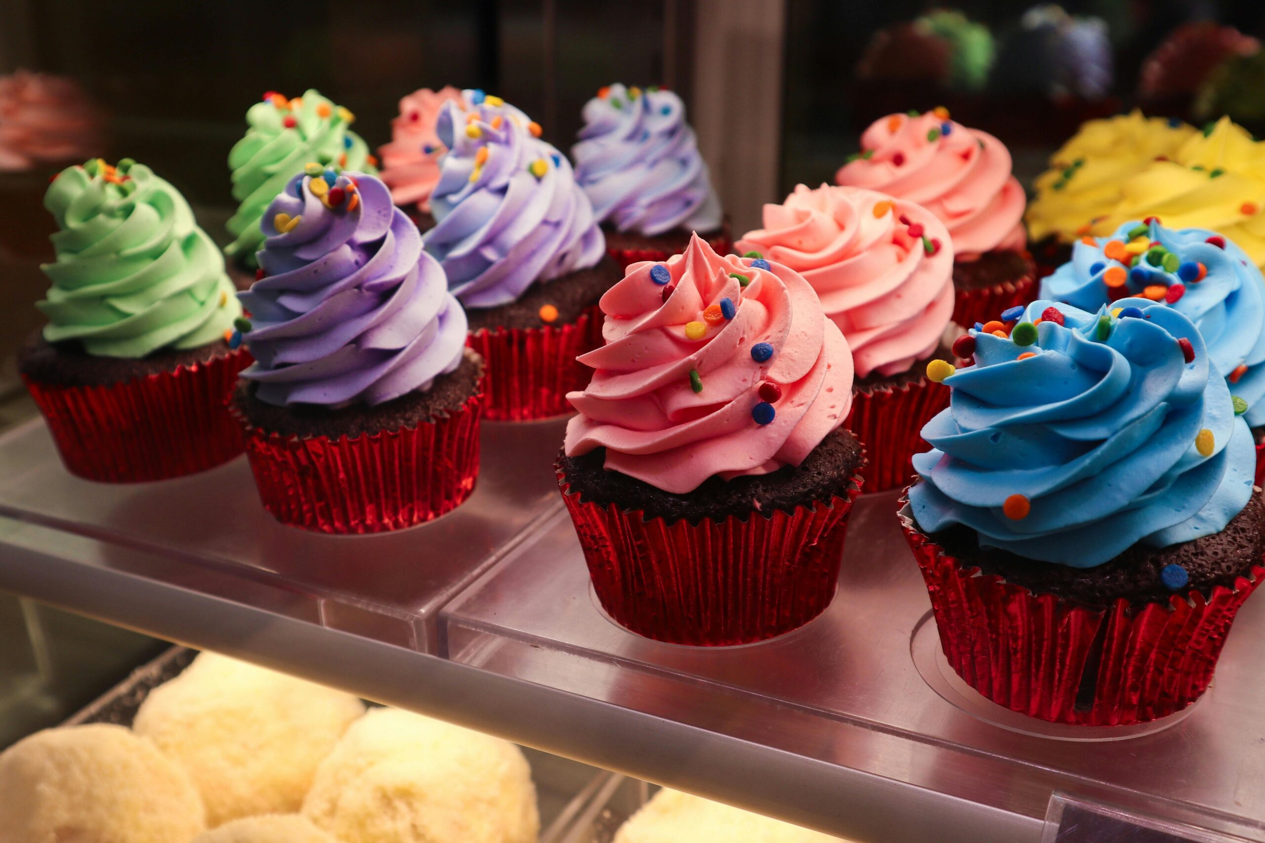 Delightful array of colorful cupcakes with vibrant icing and sprinkles in a bakery display.