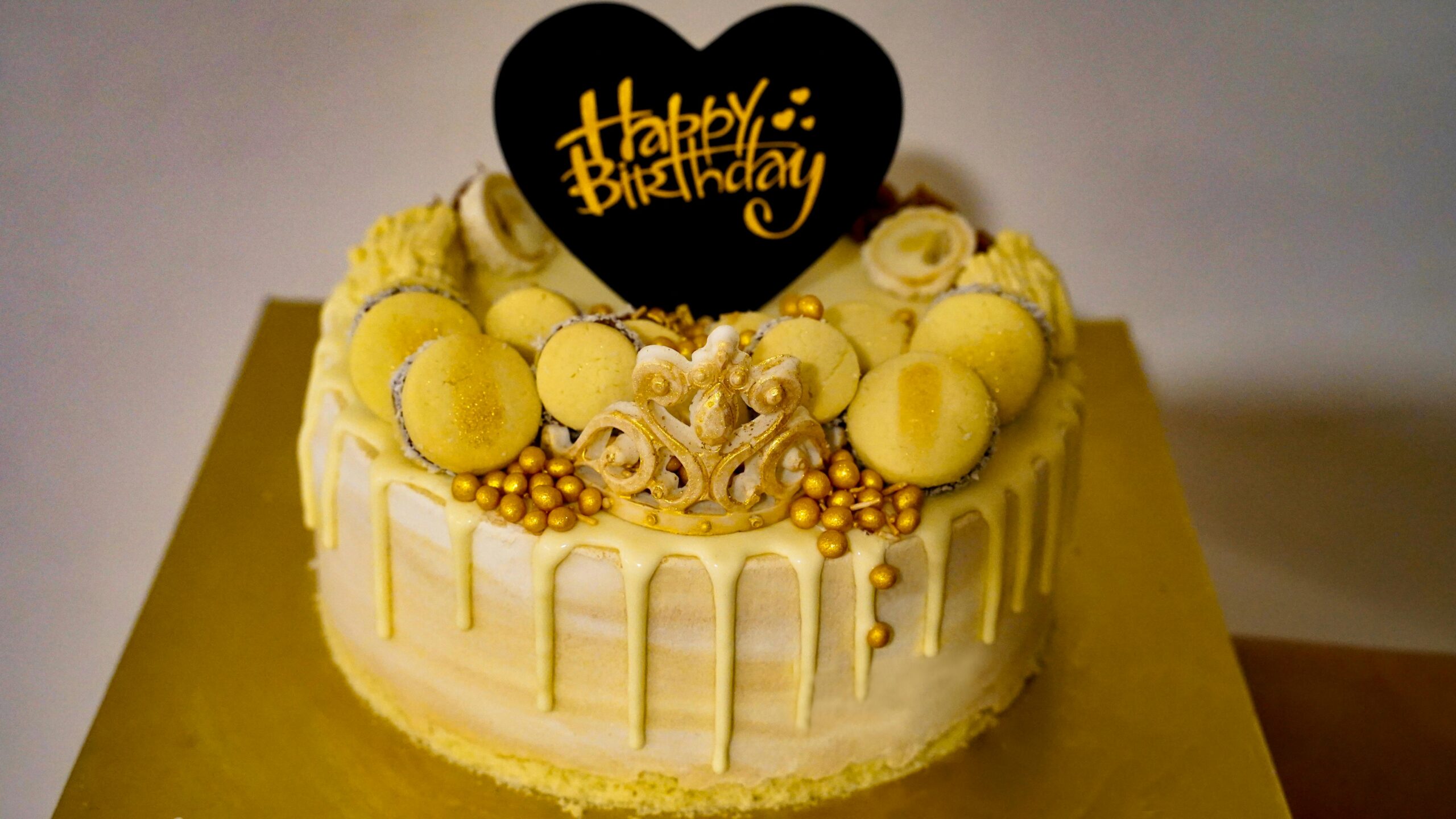 Stylish yellow birthday cake adorned with macarons and golden accents, perfect for celebrations.