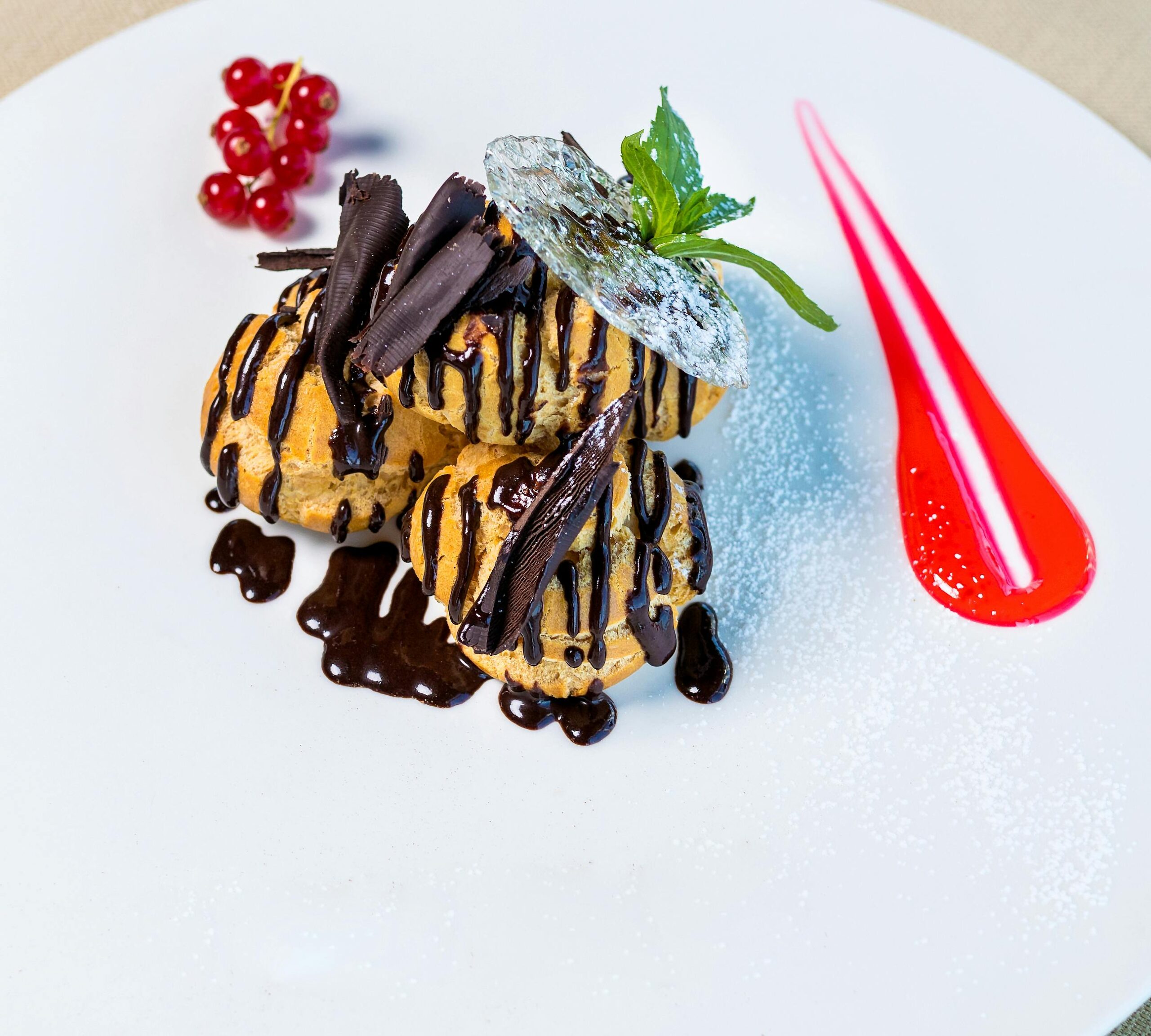 Sumptuous profiteroles topped with chocolate sauce and berries, presented on a white dish.